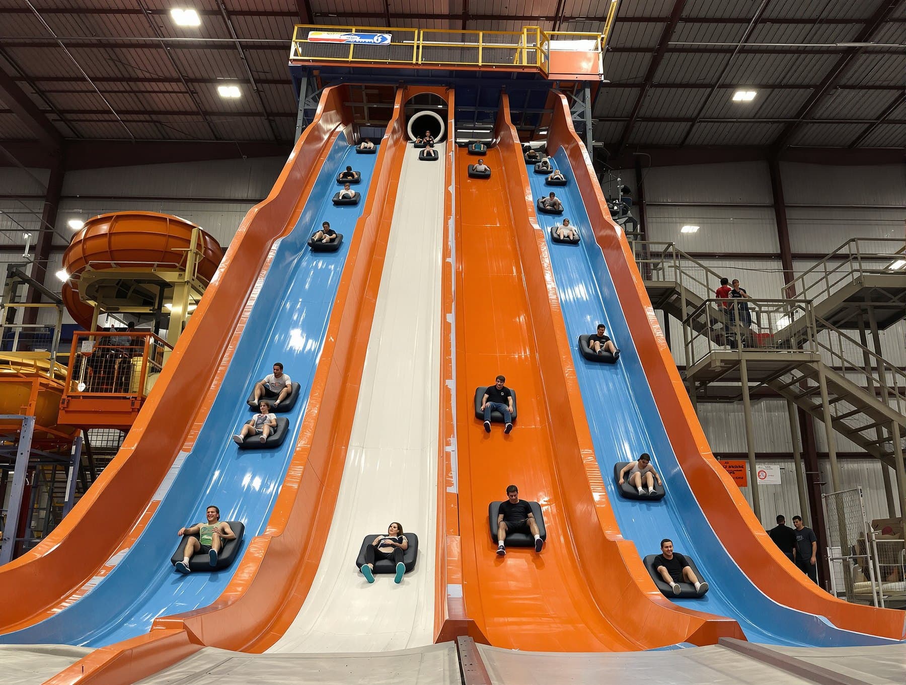 Riders racing down multi-lane indoor slides on mats